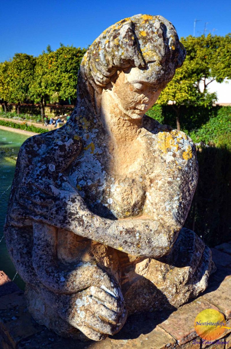 huge stone statue of woman's bust holding a child and long hair in Cordoba Alcazar gardens